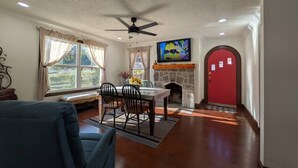 A living room with a dining area, a fireplace, a red door, and a ceiling fan. - Gingerbread Home | Quiet Stay | 30+ Day Ready (Chattanooga)