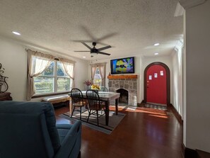 Ein Wohnzimmer mit Essbereich, Kamin, einer roten Tür und einem Deckenventilator.