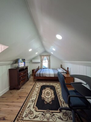 Ein Schlafzimmer mit Bett, Kommode, Fernseher und Schreibtisch mit Stuhl.