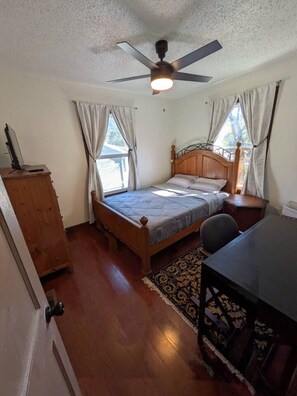 Ein Schlafzimmer mit einem Bett, einem Schreibtisch, einem Deckenventilator und einem Fenster.