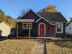 Ein Wohnhaus mit roter Tür, einer kleinen Veranda und einer gut sichtbaren Hausnummer.