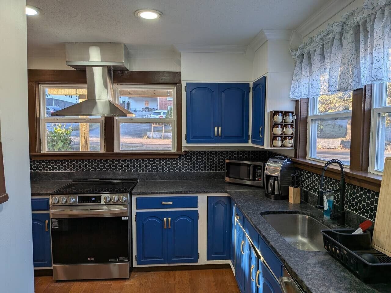 Cocina con gabinetes azules, estufa de acero inoxidable, microondas y un ventanal con vistas.