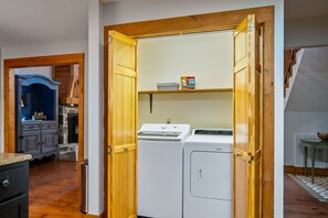 Ein Waschraum mit Waschmaschine und Trockner, Holztüren und einem Wäschekorb auf einem Regal.