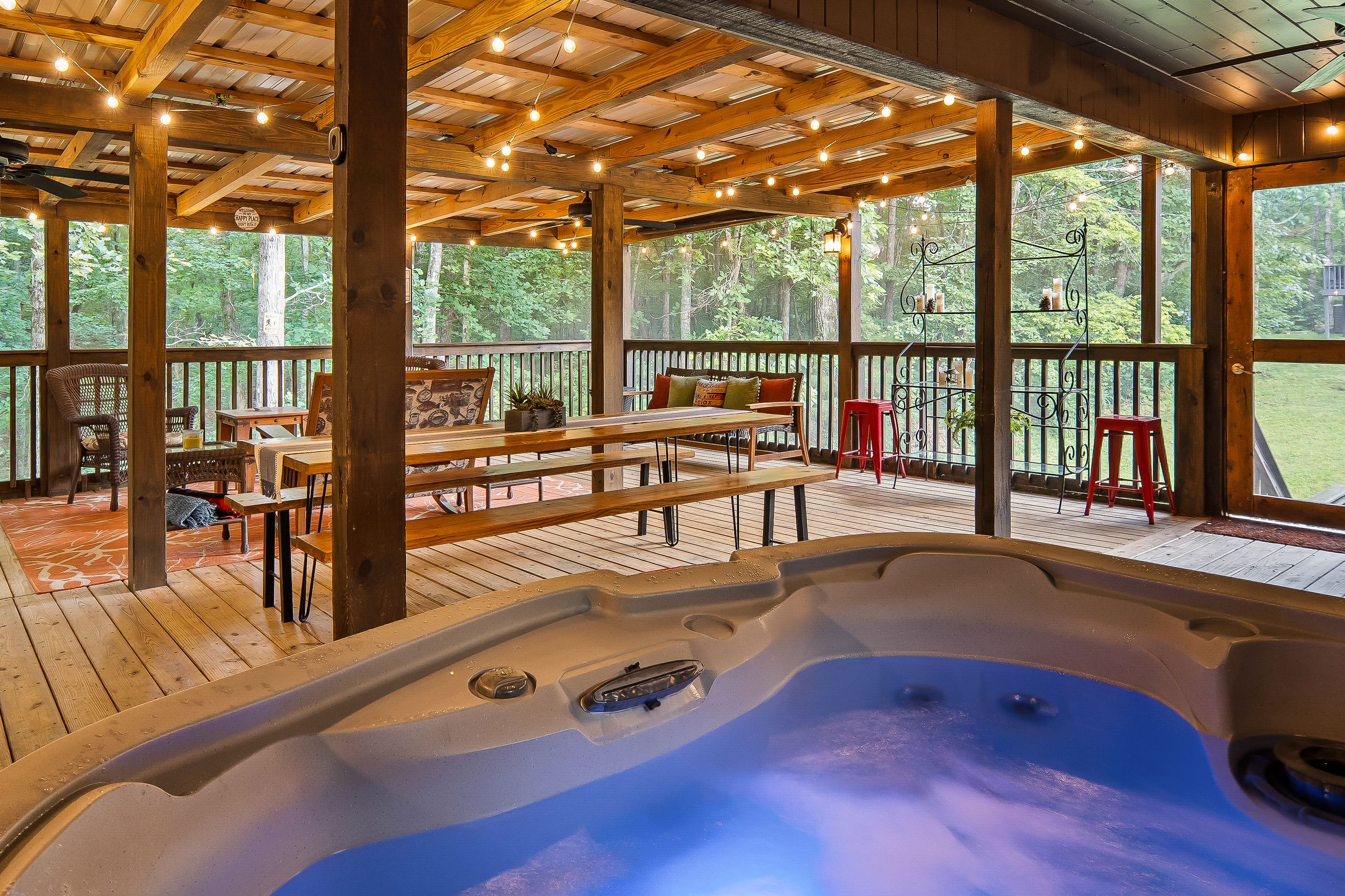 A hot tub in a wooden deck area with outdoor seating and large windows.