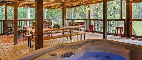 A hot tub in a wooden deck area with outdoor seating and large windows.