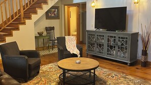 A living room with a staircase, a television, a cabinet, and a patterned rug. -  NEW LISTING 3BR CABIN NEAR FALLS CREEK FALLS, LARGE SCREENED IN PATIO HOT TUB, (Spencer)
