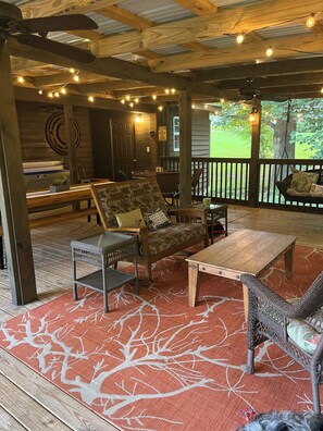Eine Terrasse im Freien mit Holzmöbeln, Lichterketten und einem roten Teppich mit Muster.
