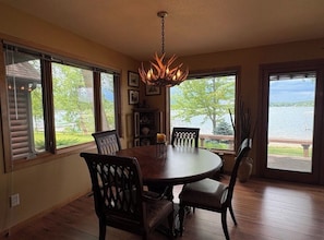 A dining area with a round table and chairs, a chandelier, and large windows with a view of a body of water.