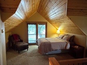 A bedroom with a sloped ceiling, a bed, a chair, and a nightstand.