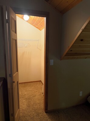 A room with a wooden ceiling, a closet with hanging clothes, and a carpeted floor.