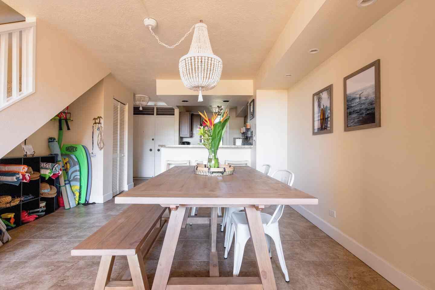 A dining area with a wooden table, white chairs, a chandelier, and a view of the kitchen.