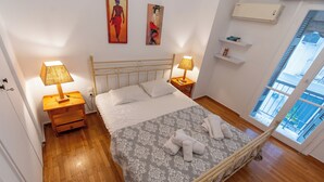A bedroom with a bed, two bedside tables with lamps, a wardrobe, and a window with a view. -  Live Like a Local, Steps From Acropolis | Homey, Roomy & Sleeps 4 (Athina)