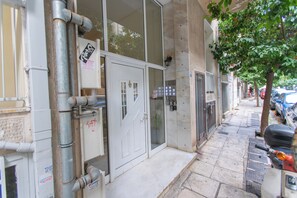 A building facade with a door, windows, and a small tree on the sidewalk. -  Live Like a Local, Steps From Acropolis | Homey, Roomy & Sleeps 4 (Athina)