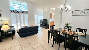 A modern living room with a sofa, a dining table set for four, and a television in the background. - Lovely home, Quiet Escape Near Disney (Kissimmee)
