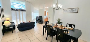 A modern living room with a sofa, a dining table set for four, and a television in the background. - Lovely home, Quiet Escape Near Disney (Kissimmee)