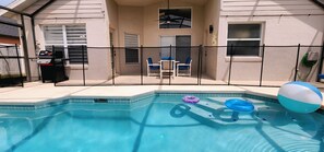 A swimming pool with a fence, a grill, and a door leading to a covered patio area. - Lovely home, Quiet Escape Near Disney (Kissimmee)