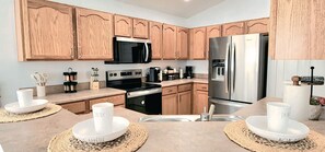 A modern kitchen with wooden cabinets, stainless steel appliances, and a central island with placemats. - Lovely home, Quiet Escape Near Disney (Kissimmee)