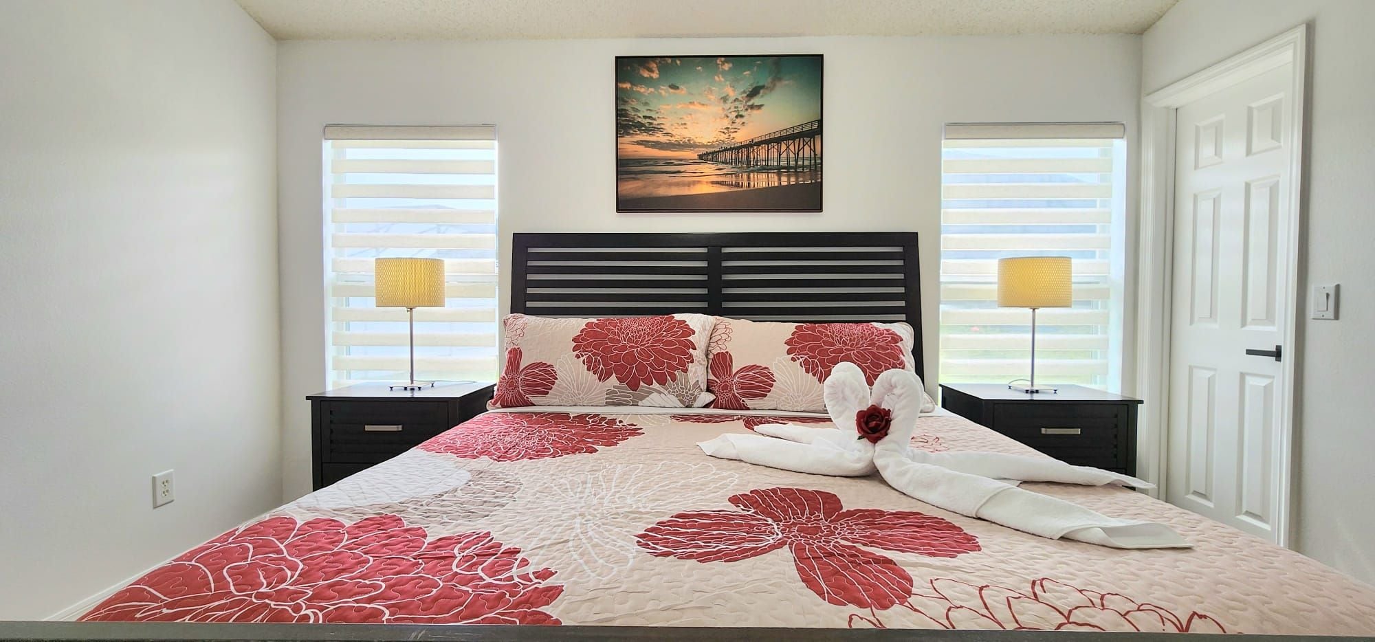 A bedroom with a bed, two nightstands, a painting, and a door.