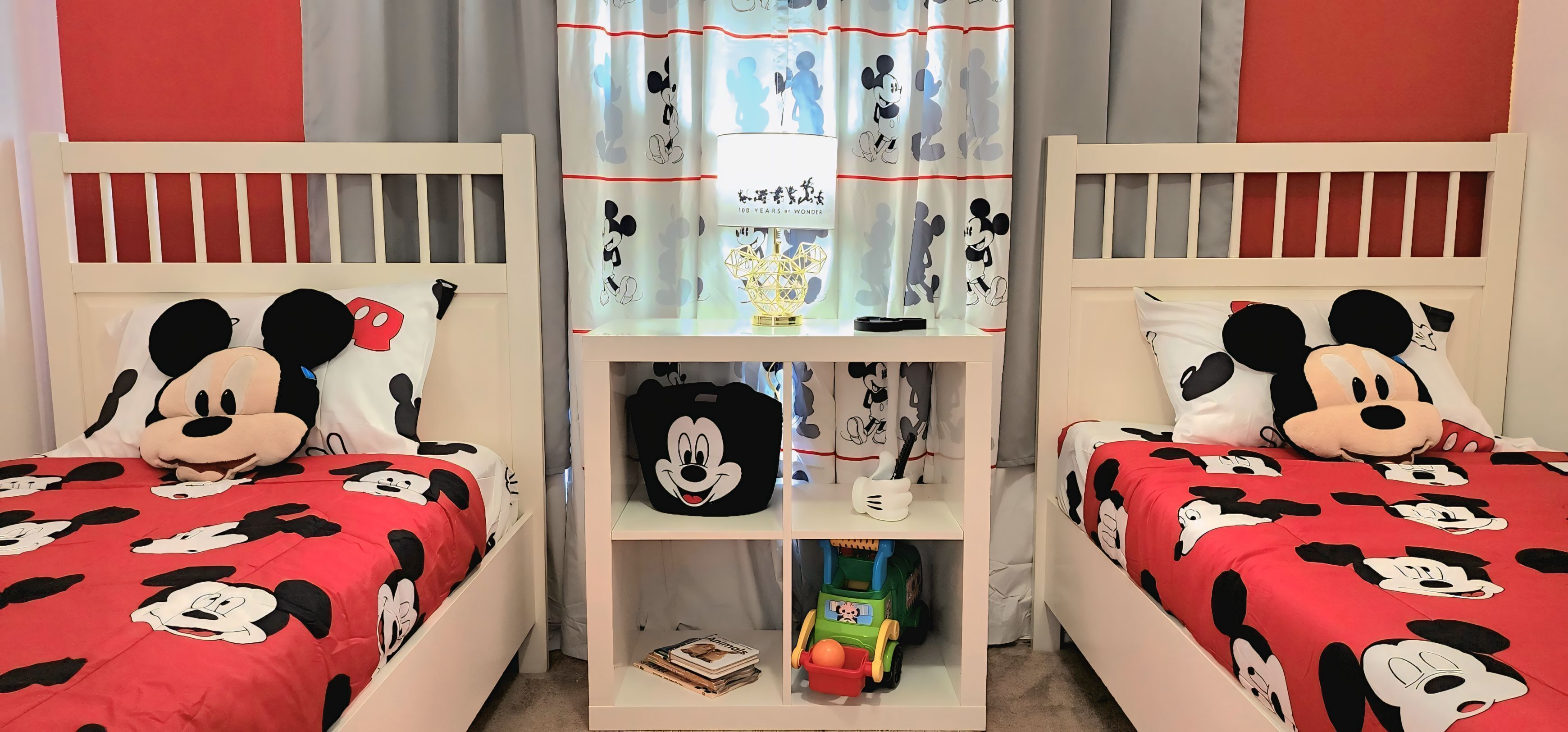 Zwei Doppelbetten mit Mickey Mouse Bettwäsche, ein Nachttisch mit einem Mickey Mouse Kopfkissen und ein Regal mit Artikeln passend zum Thema Mickey Mouse.