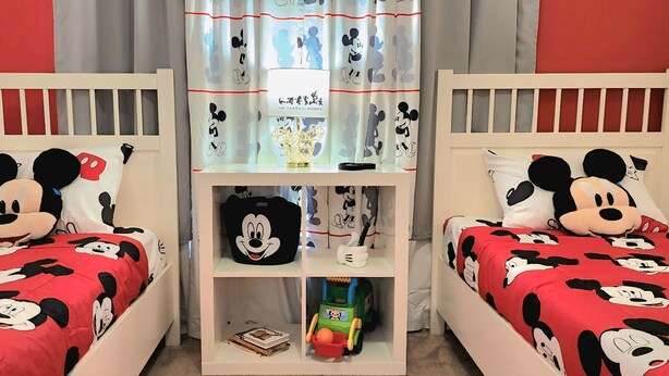 Two twin beds with Mickey Mouse bedding, a nightstand with a Mickey Mouse pillow, and a shelf with Mickey Mouse-themed items. - Lovely home, Quiet Escape Near Disney (Kissimmee)