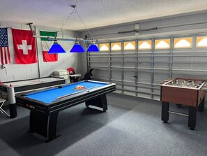 A recreational room with a pool table, foosball table, and two flags on the wall. - Lovely home, Quiet Escape Near Disney (Kissimmee)