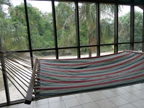 A hammock in a room with large windows overlooking a tropical garden. - Authentic Sarteneja– Pool, Birds & Tranquility (Sarteneja)