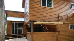 A wooden cabin with a gravel driveway, a covered porch, and a metal gate.