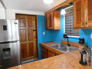 A kitchen with a stainless steel refrigerator, wooden cabinets, a sink, and a window with blinds.