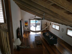 A spacious living area with a hammock, wooden floors, a sofa, and a ceiling fan. - Authentic Sarteneja– Pool, Birds & Tranquility (Sarteneja)