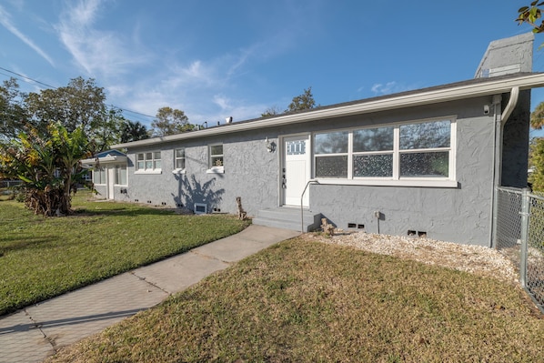 A two-story residential building with a grey exterior, a front porch, and a small front yard with a pathway leading to the entrance.