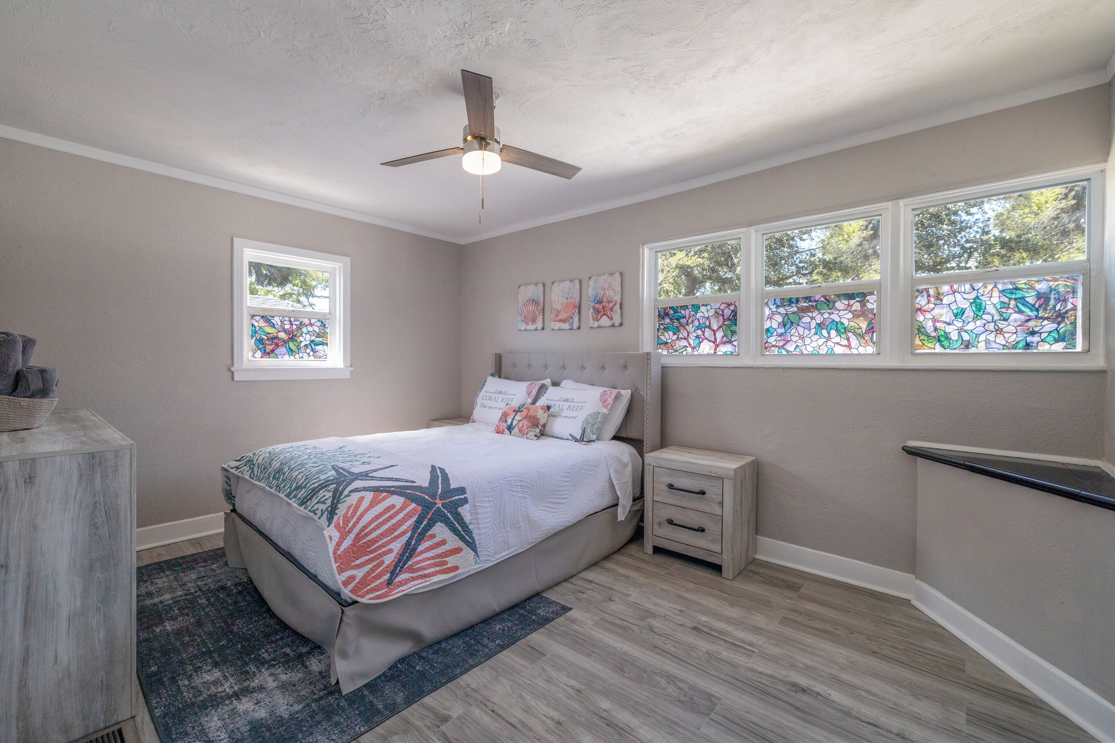 A bedroom with a bed, nightstands, a ceiling fan, and windows with stained glass.