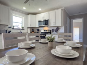 A modern kitchen with white cabinets, a microwave, oven, and a dining table set with white bowls and plates.