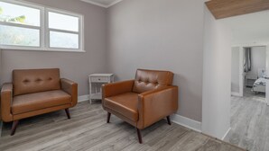A room with two leather armchairs, a small white side table, and a window with a view of trees.