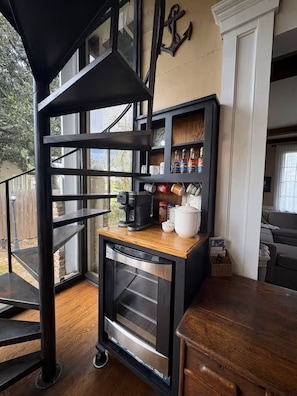 A compact kitchen with a built-in oven, a coffee maker, and a shelf with various kitchen items.