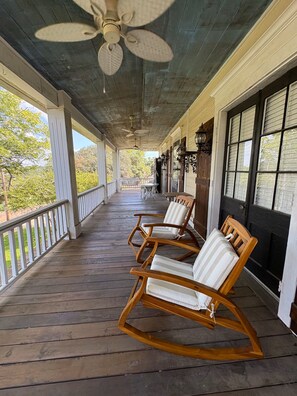 A covered porch with wooden flooring, ceiling fans, and outdoor seating with cushioned chairs.