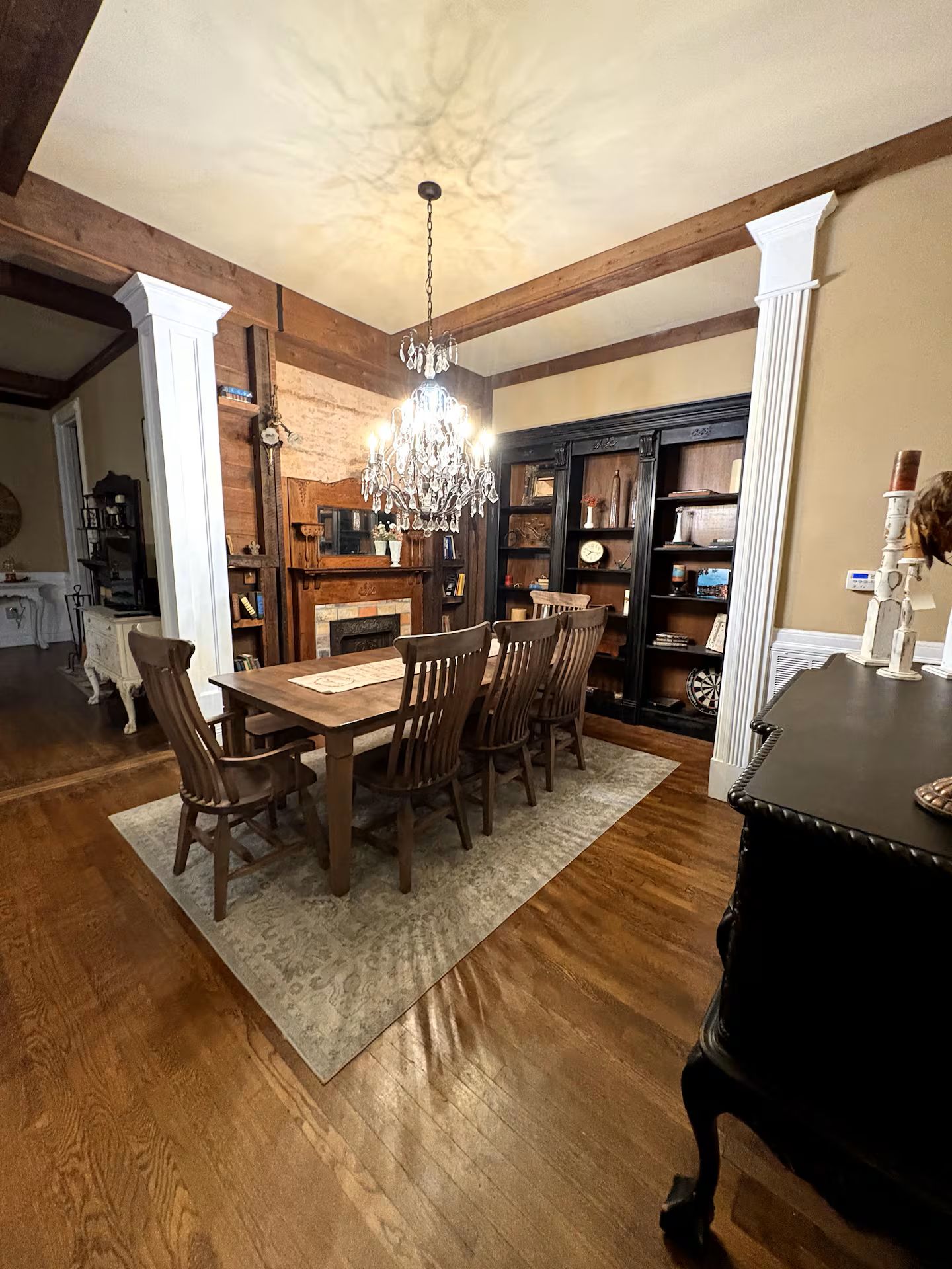 A dining area with a wooden table and chairs, a chandelier, and a fireplace.