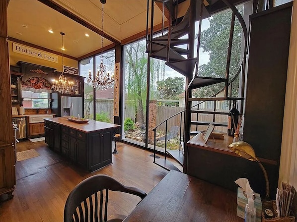 A modern kitchen with a central island, a chandelier, and a view of the backyard through large windows.