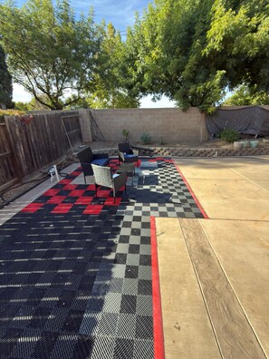 An outdoor patio with a checkered floor, a wooden fence, and a brick wall. - Spacious 4-Bedroom House /Self Check-In/Wifi/King Bed/EV Charger/Newly Renovated (Modesto)