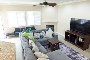 A living room with a sectional sofa, a television on a stand, a fireplace, and two windows with blinds. - Spacious 4-Bedroom House /Self Check-In/Wifi/King Bed/EV Charger/Newly Renovated (Modesto)