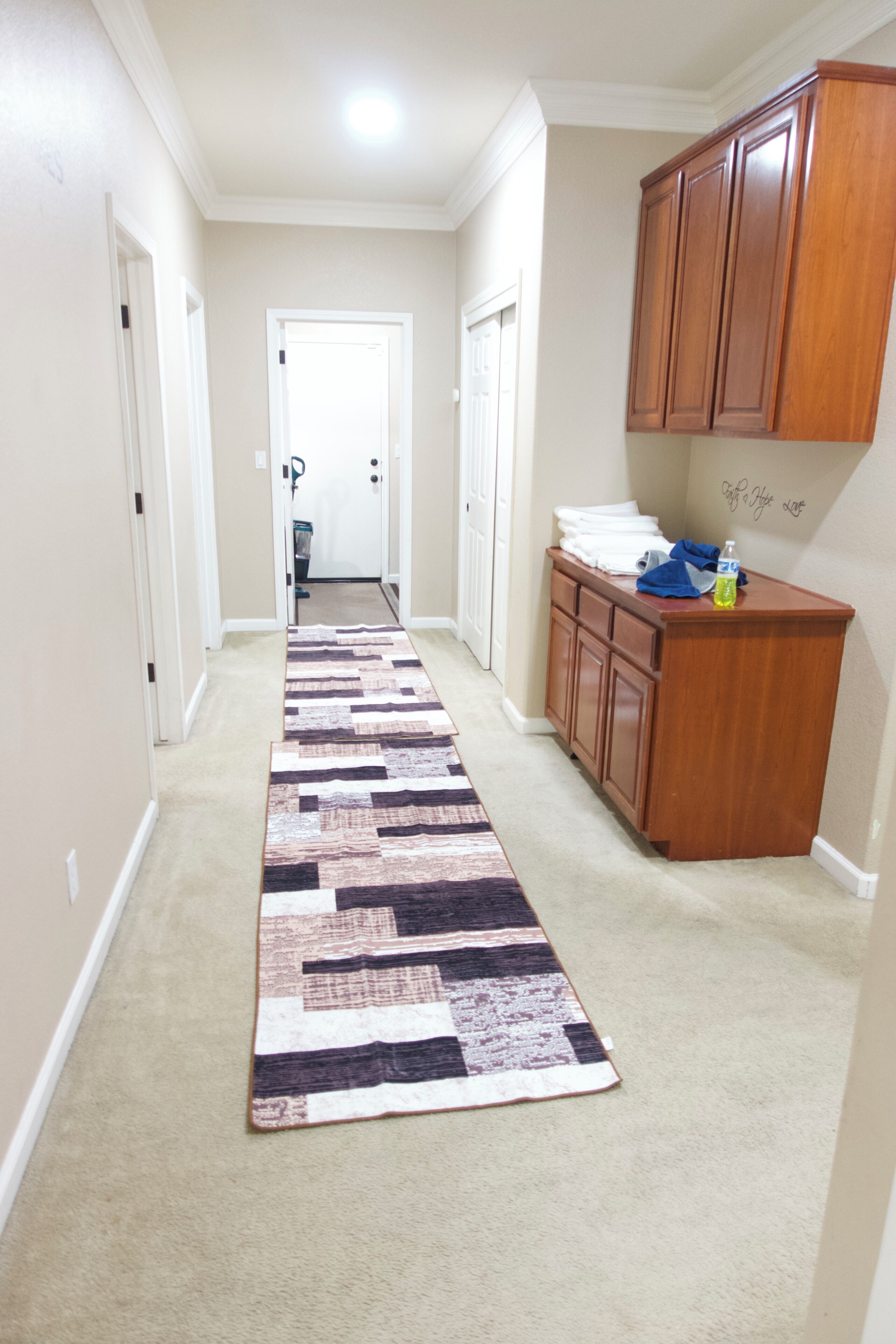 A hallway with a carpet, wooden cabinets, and a door leading to another room.