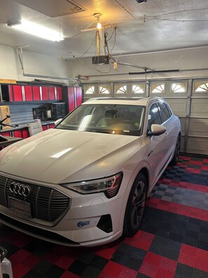 A white Audi car in a garage with red lockers and a patterned floor. - Spacious 4-Bedroom House /Self Check-In/Wifi/King Bed/EV Charger/Newly Renovated (Modesto)