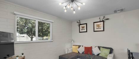 A modern living room with a sectional sofa, two side tables, a flat-screen TV, and a ceiling light fixture.