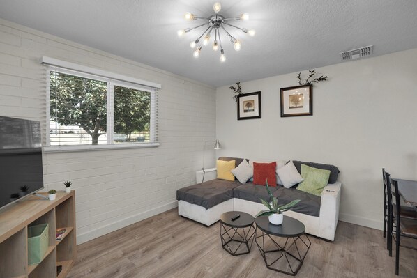 A modern living room with a sectional sofa, two side tables, a flat-screen TV, and a ceiling light fixture.
