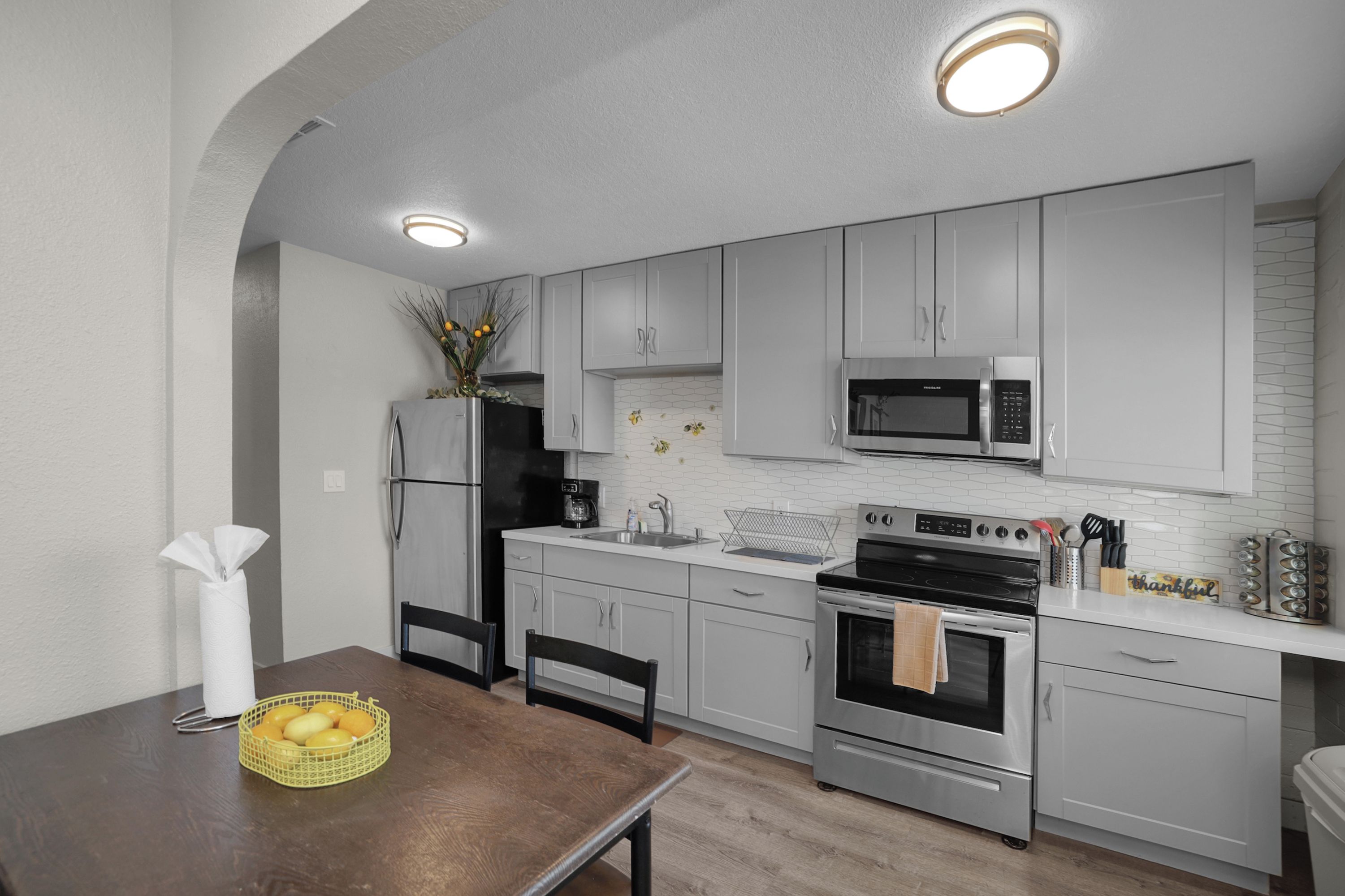 Una cocina moderna con armarios blancos, un refrigerador de acero inoxidable, un microondas, una estufa y un lavamanos.