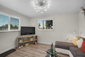 A living room with a flat-screen TV, wooden shelving, a plant, a sofa, and a ceiling light fixture.