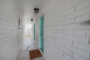 A corridor with white brick walls, a teal door, and a brown mat at the entrance.