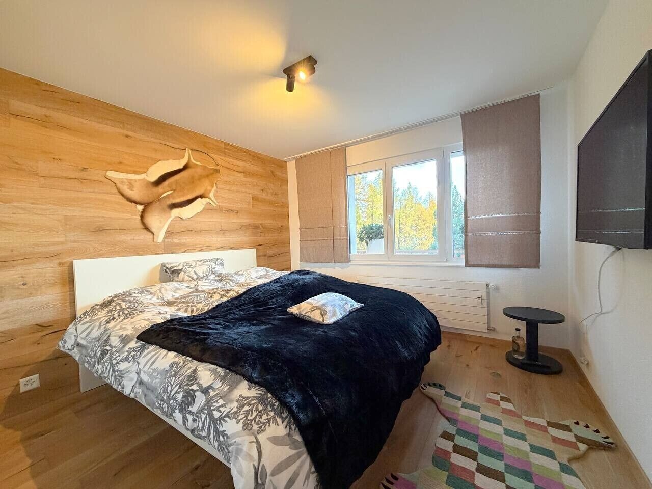 A bedroom with a bed, a wooden headboard, a window with blinds, a television, and a small round table.