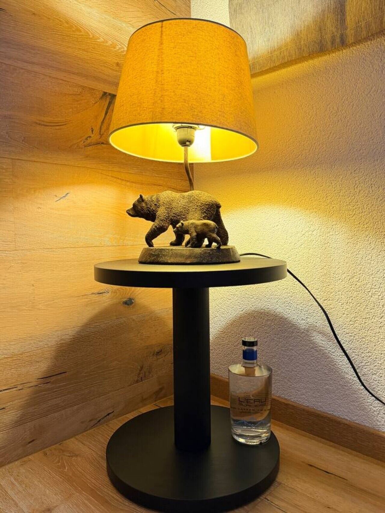 Una lámpara con una figurita de oso sobre una mesa, una botella de agua y un muro de madera.