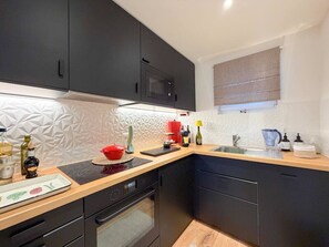 A modern kitchen with dark cabinetry, a microwave, a sink, and a window with a blind. - Beautiful apartment in a prime location in Crans-Montana (Crans-Montana)