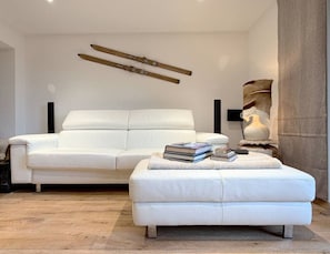 A modern living room with a white sofa, a white ottoman, and a decorative wall piece. - Beautiful apartment in a prime location in Crans-Montana (Crans-Montana)